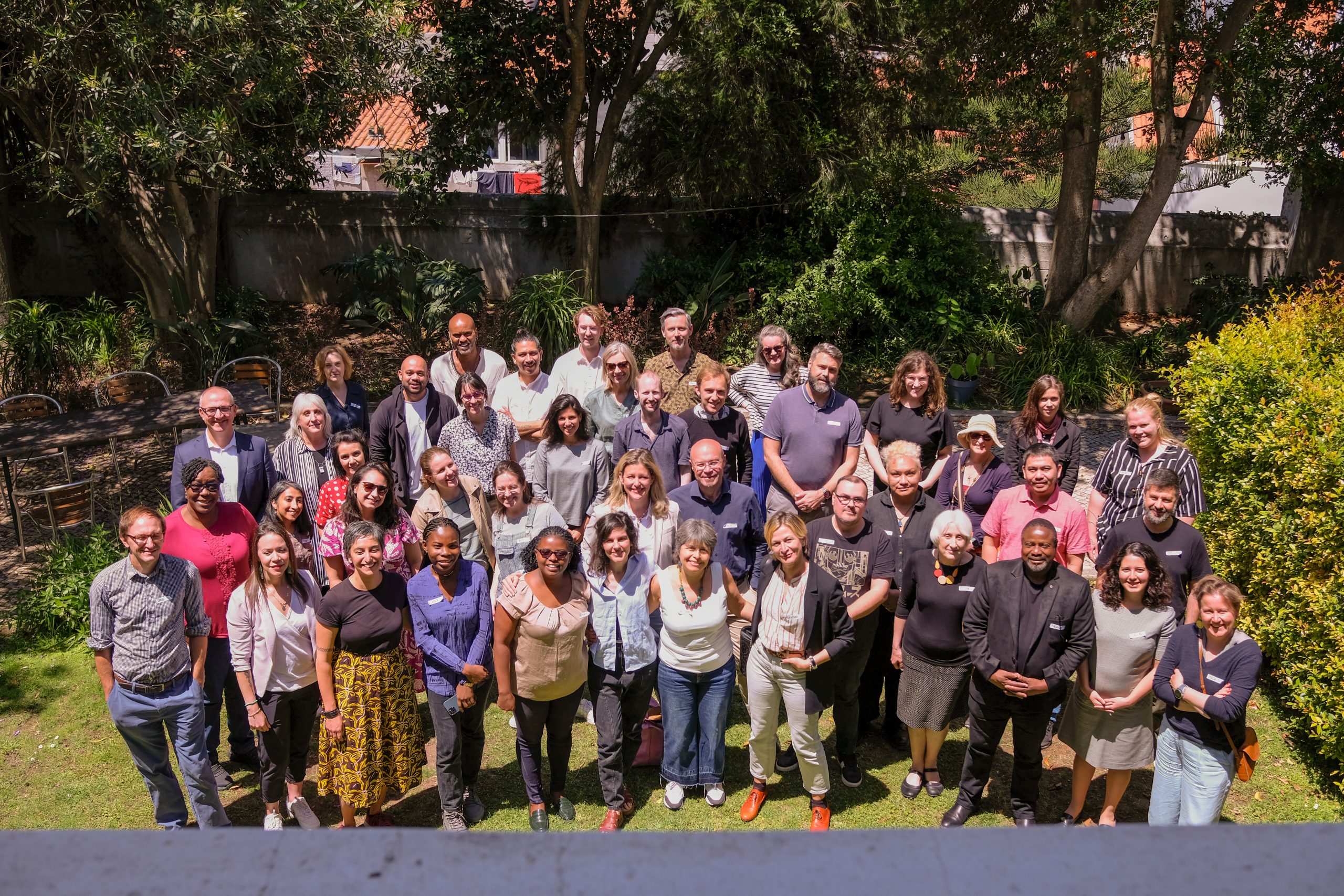 A group of people standing together looking at the camera in a green garden. 